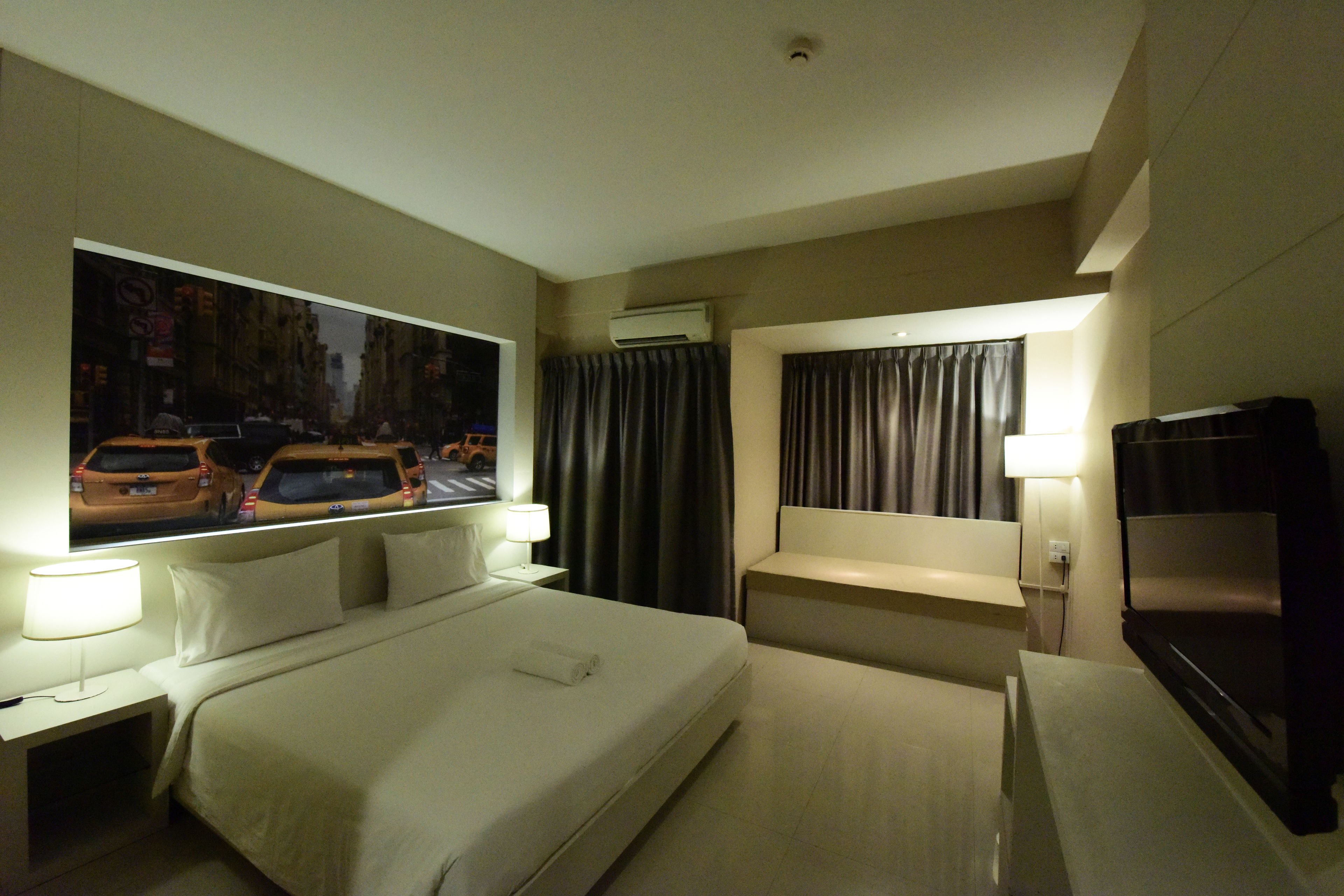 A hotel room with a large bed, a TV, a desk, and a window with a cityscape view.