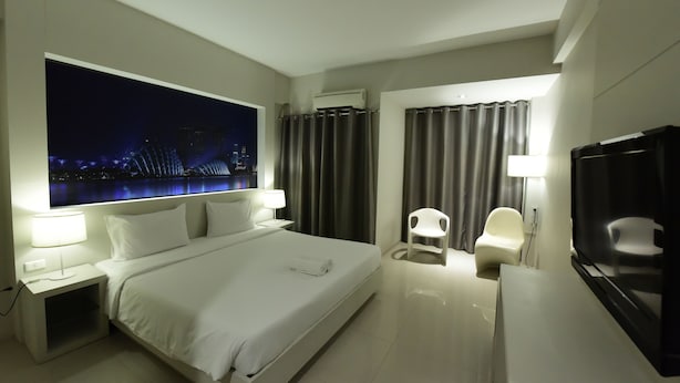 Una habitación de hotel moderna con una cama grande, un televisor de pantalla plana, un escritorio con silla y un ventanal con cortinas.