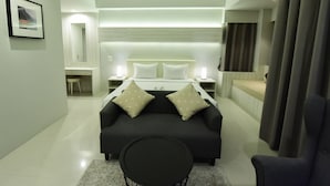 Una habitación de hotel moderna con una cama grande, mesitas de noche, una pequeña zona de estar y vistas a la ciudad.
