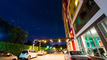 Un estacionamiento con varios coches, un edificio con amplias ventanas y un pasillo cubierto.