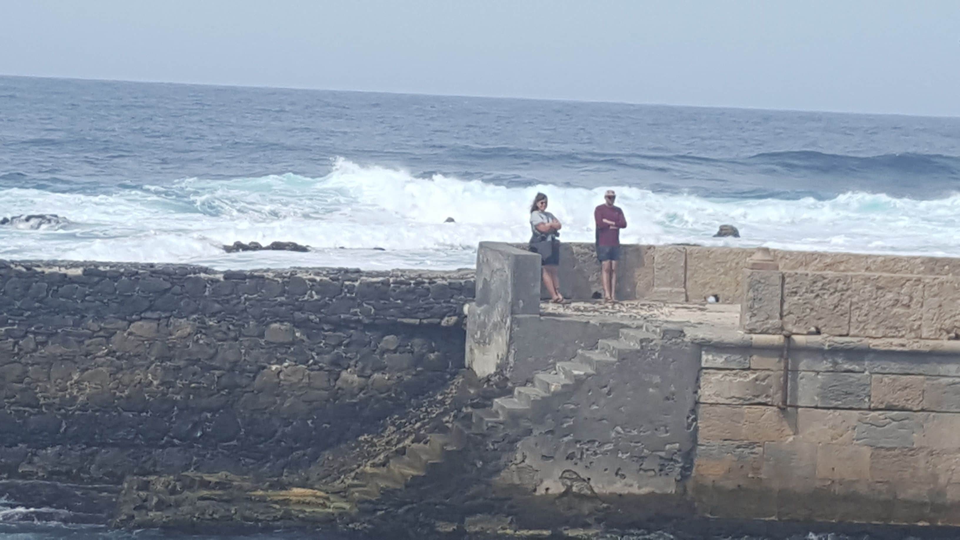 A stone pier extending into the ocean with two people standing at the end.