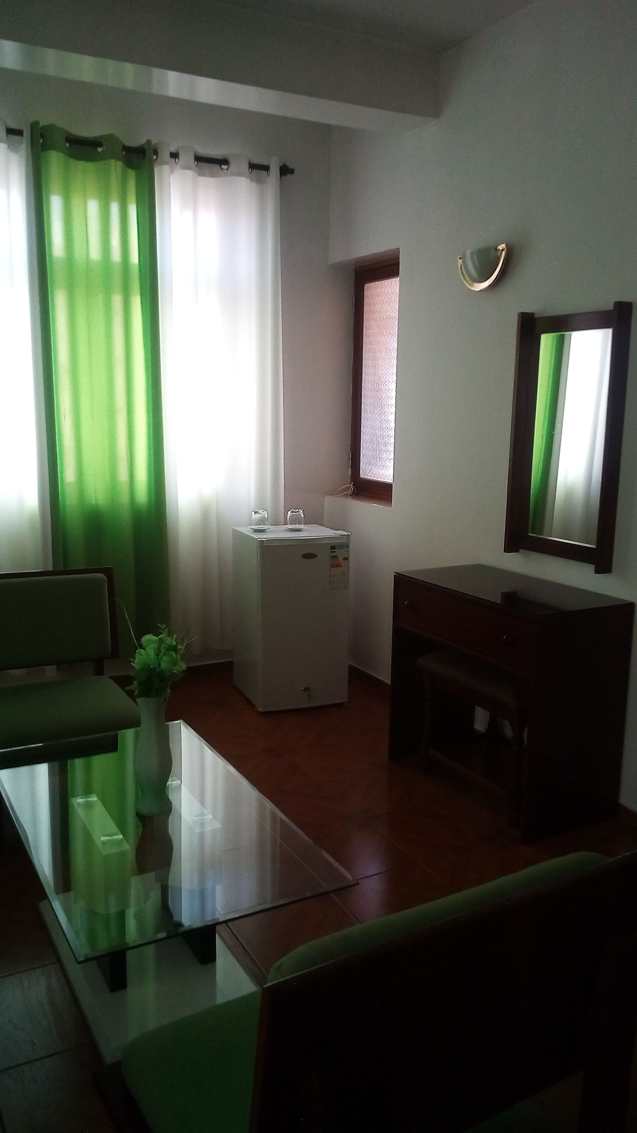 Un espacio habitable compacto con una mesita de centro de vidrio, un sofá, un refrigerador pequeño y una ventana con vistas.