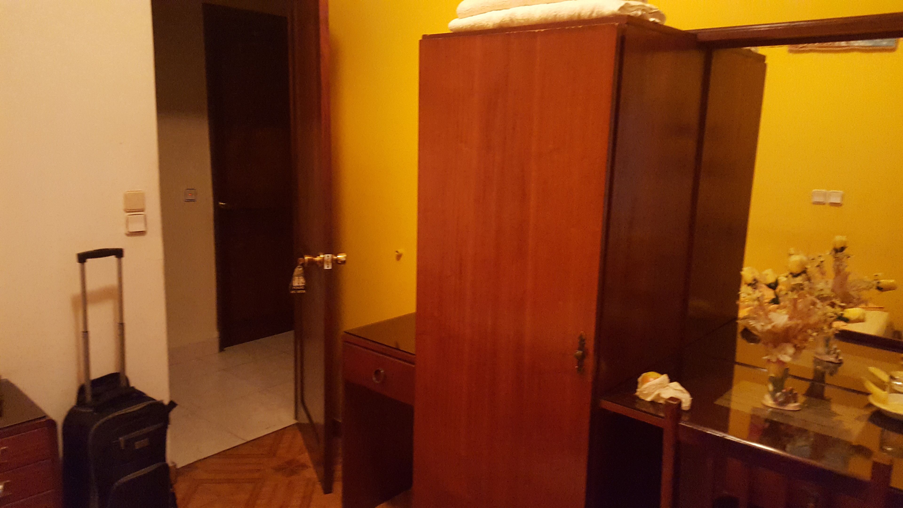 Una habitación de hotel con un armario de madera, una mesita con un florero y una maleta.