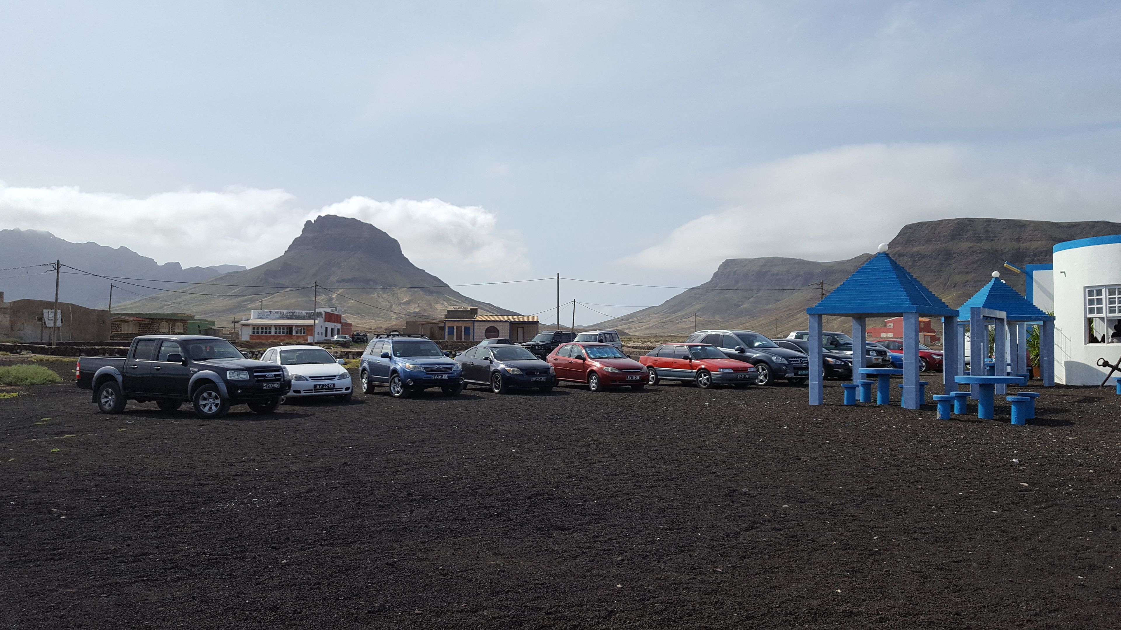 A parking area with various cars, a blue play structure, and buildings in the background.