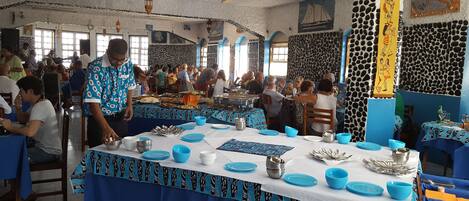 Un espace de restauration commun avec des tables dressées pour le repas, agrémenté d’une nappe à motifs et d’assiettes bleues et blanches.