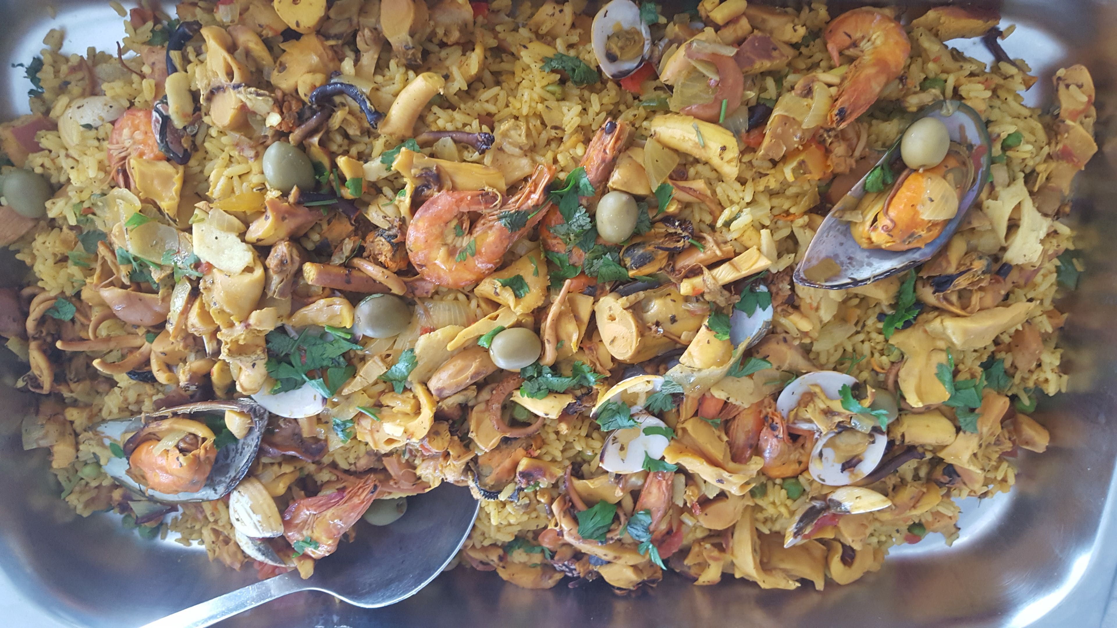 A large metal serving dish filled with seafood paella, featuring shrimp, mussels, and clams.
