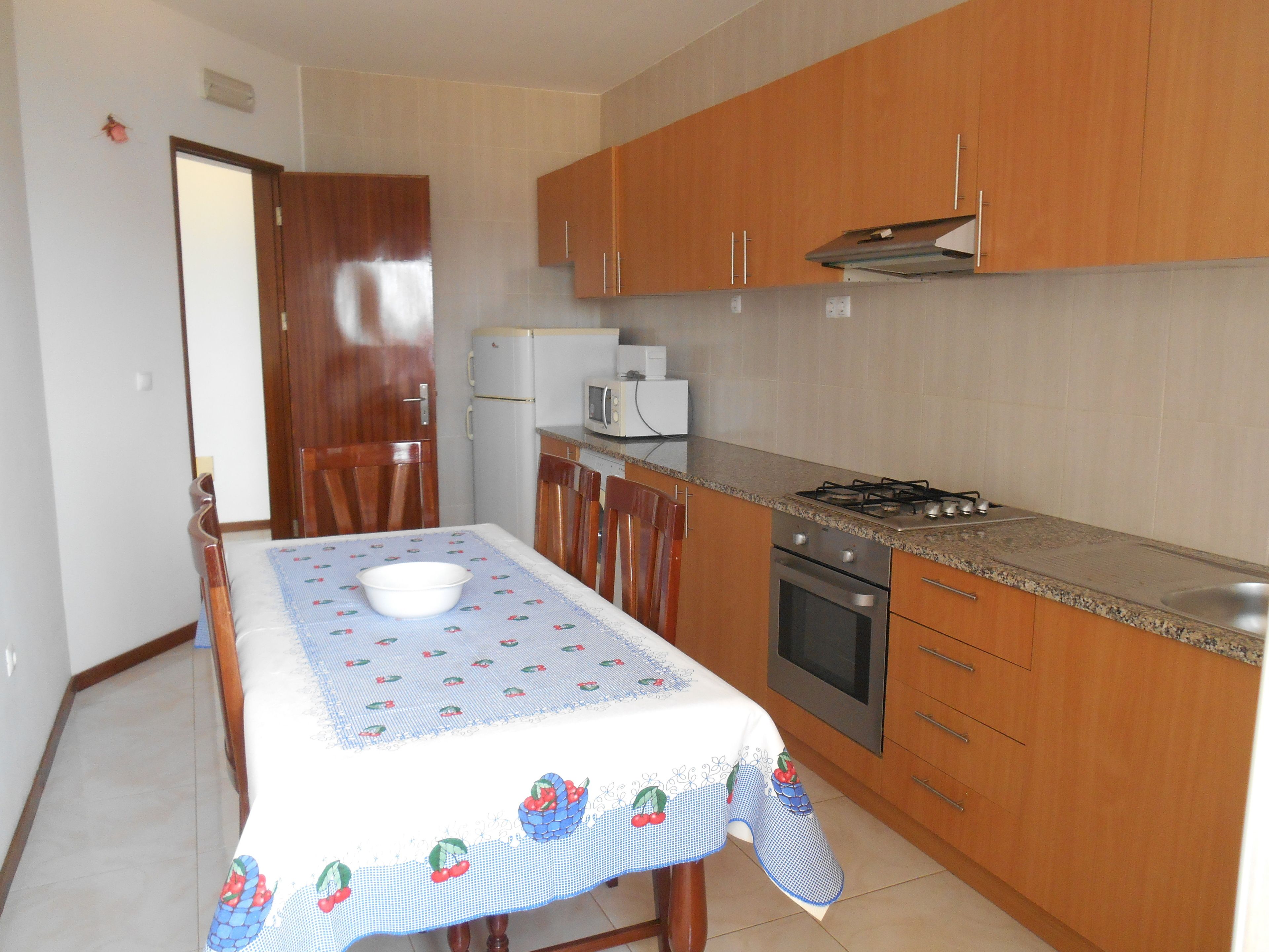 A compact kitchen with wooden cabinets, a gas stove, a microwave, and a refrigerator.