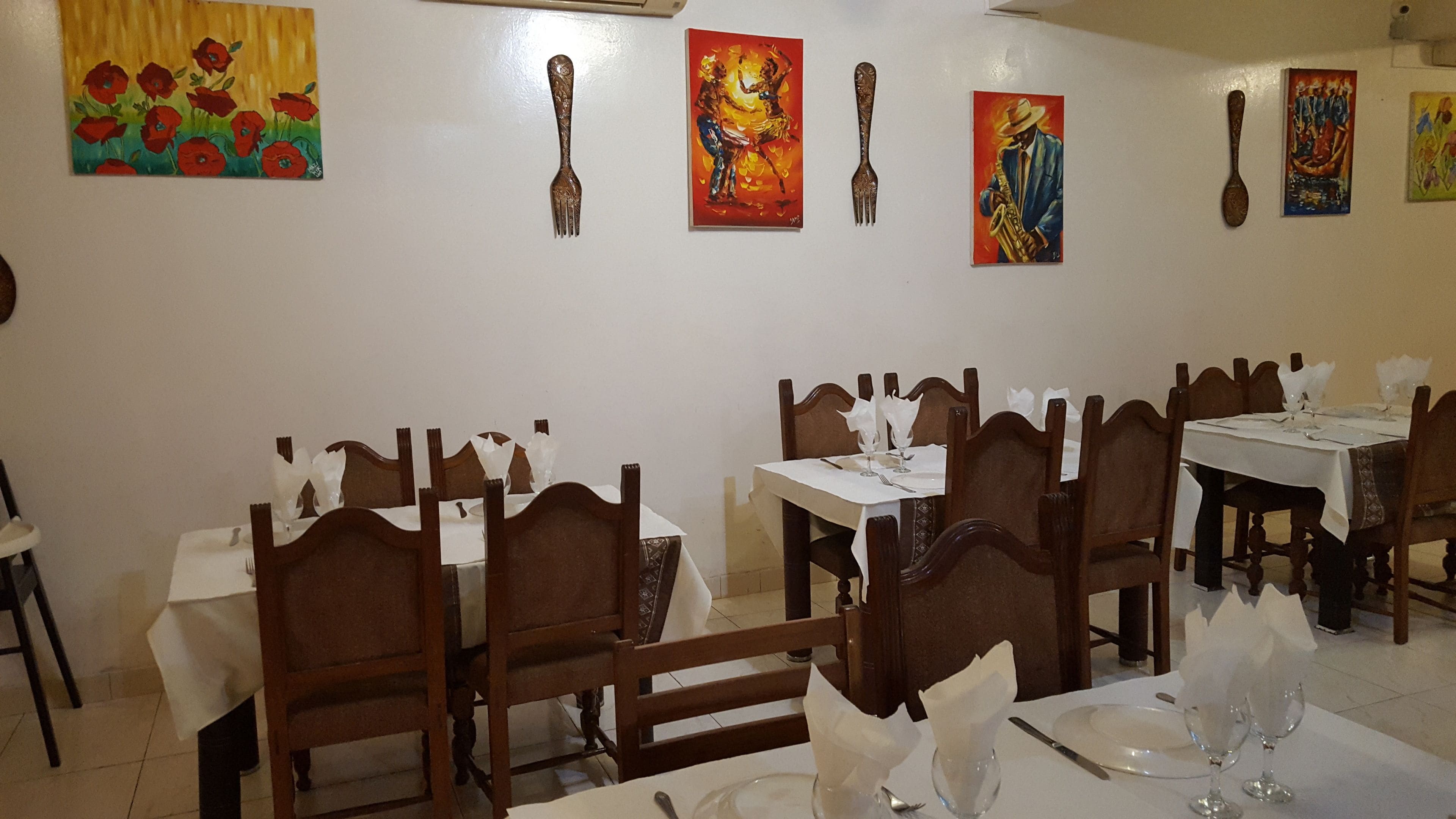 A dining area with tables set for four, wooden chairs, and artwork on the walls.