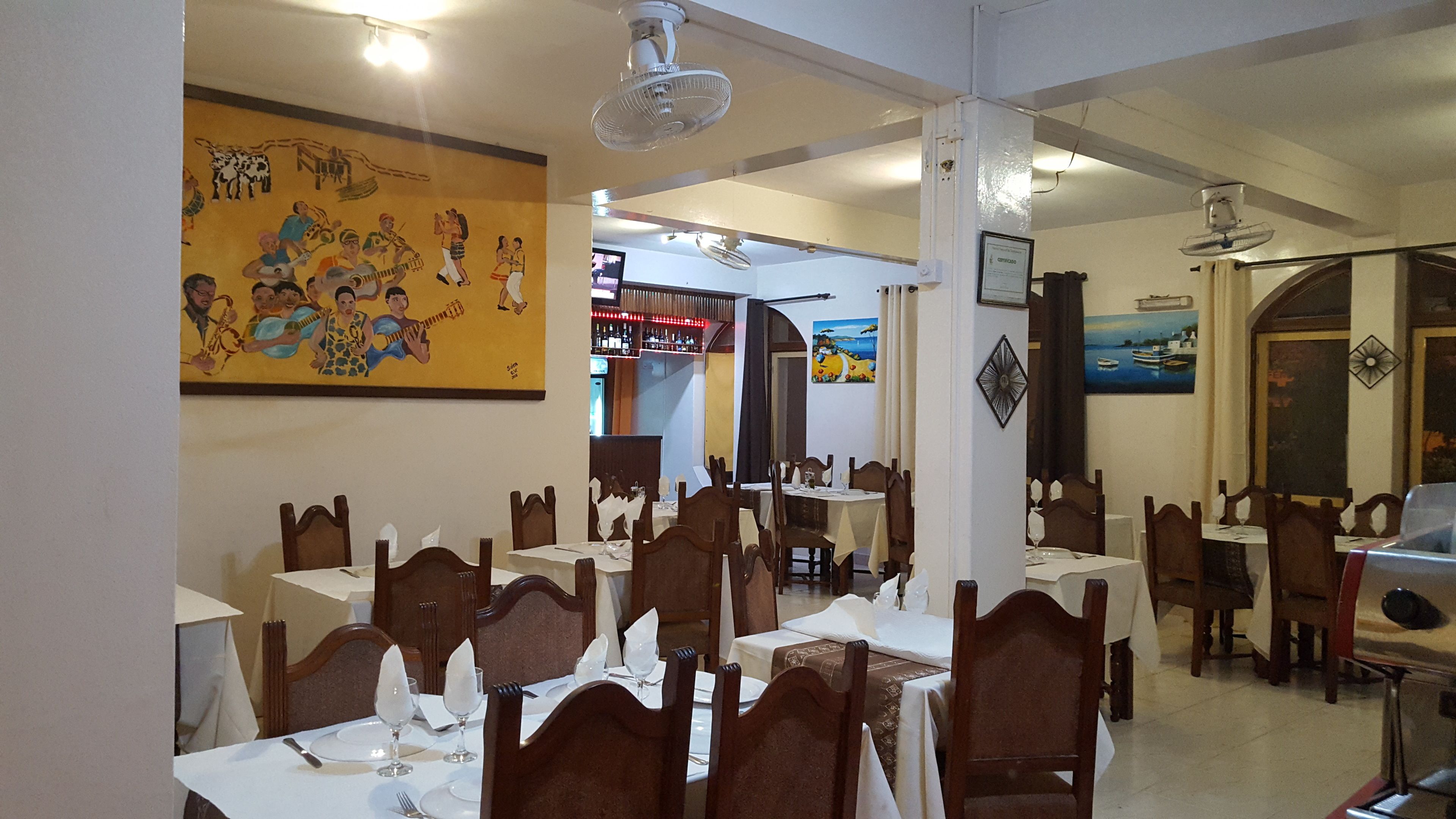 Ein Restaurantinneres mit mehreren gedeckten Tischen, Holzstühlen und einem Wandgemälde.