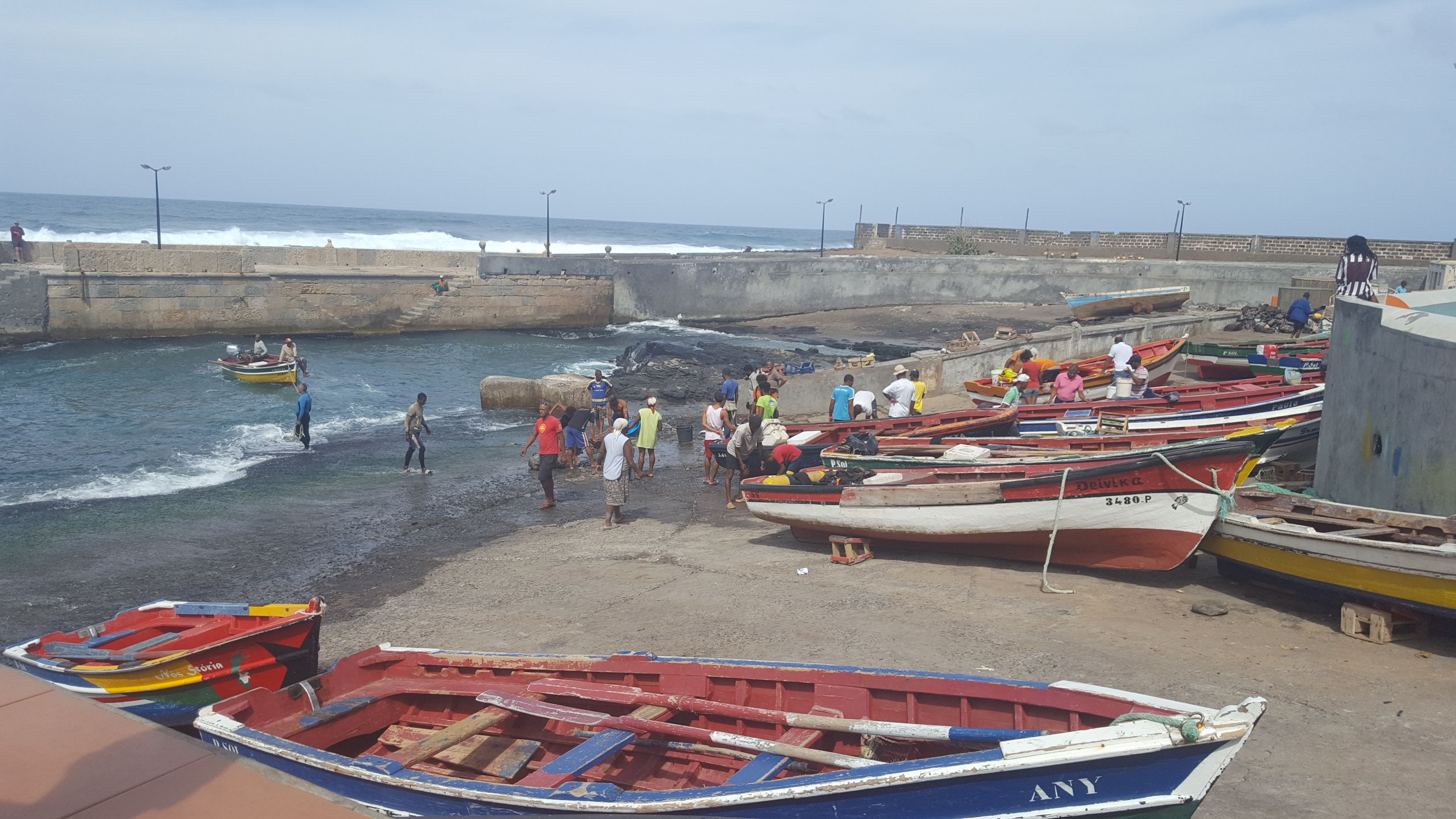 A beachside pier with several boats docked and people walking along the shore.