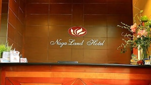 Mostrador de recepción del Hotel Naga Land, con un logotipo, el nombre del hotel y algunos objetos sobre el mostrador.