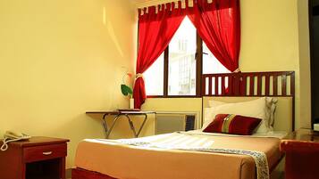 Habitación de hotel con cama, escritorio, silla, teléfono y ventana con cortinas rojas.