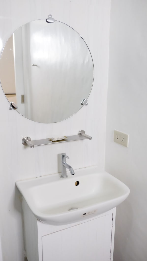 A bathroom with a white sink, a round mirror, and a towel rack.