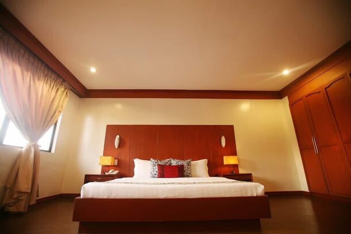 A hotel room with a large bed, wooden headboard, two bedside tables with lamps, and a wardrobe.