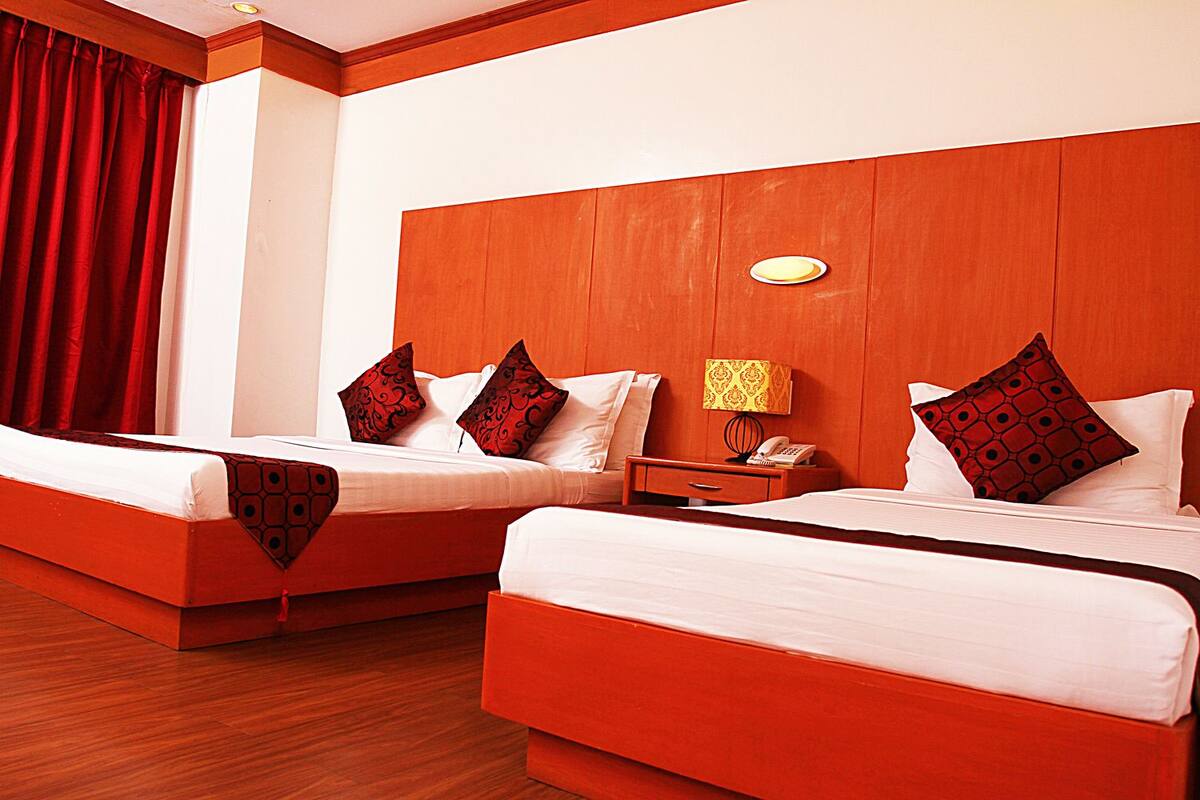 A hotel room with two beds, a wooden headboard, a nightstand with a lamp, and a red curtain.