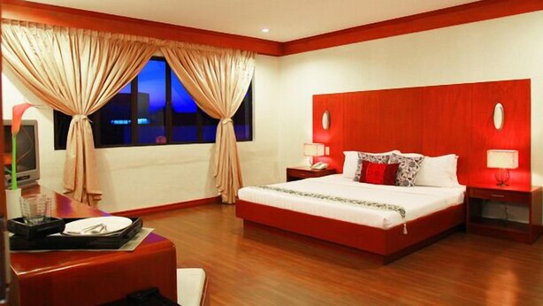 Habitación de hotel con una cama grande, un escritorio con una silla, un televisor y una ventana con cortinas.