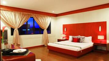 Relax in a stylish room with a large bed, bedside table, and TV on a stand, plus a large window with curtains.