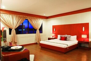 Habitación de hotel con una cama grande, un escritorio con una silla, un televisor y una ventana con cortinas.