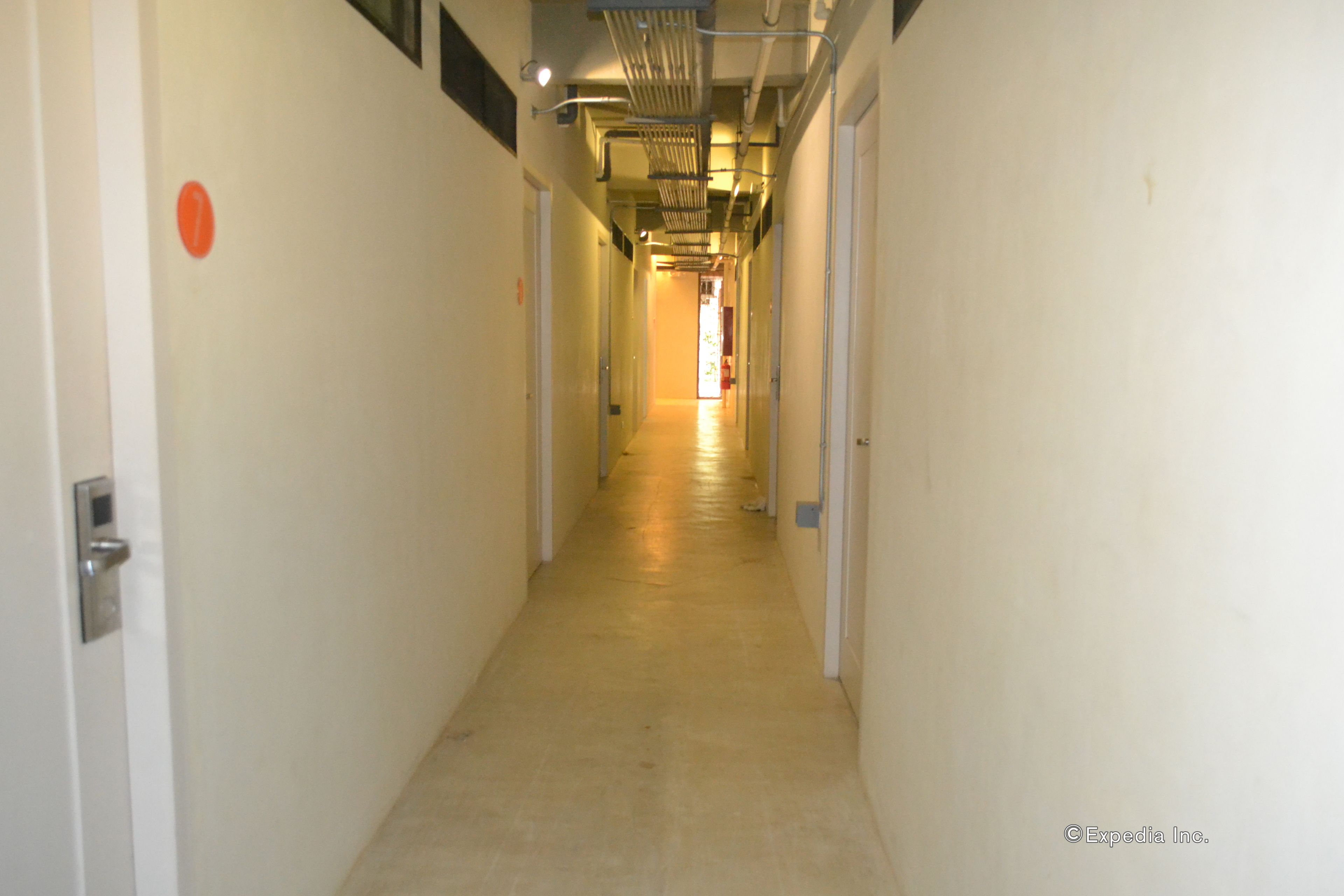A narrow, well-lit hallway with white walls and a tiled floor, leading to a door at the end.