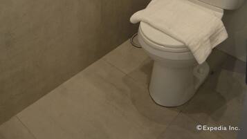 A bathroom with a toilet, a towel on the seat, and a wooden rack on the wall.