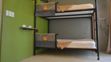 Un lit superposé à deux niveaux, chaque niveau étant équipé d’un oreiller et d’une couverture. Des étagères sont fixées au mur au-dessus des lits.