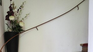 A wooden staircase with red carpet runners and a black vase with flowers on a white wall. - Pension Alt-Strassgang (Graz)