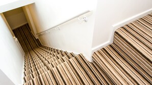 A carpeted staircase with a striped pattern, white walls, and a door leading to a room. - Trivelles Hotels - Eccles New Road (Salford)
