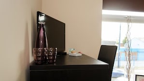 A dark wooden desk with a flat-screen TV, two glasses, and a small tray with a tissue box and a bottle. - Trivelles Hotels - Eccles New Road (Salford)