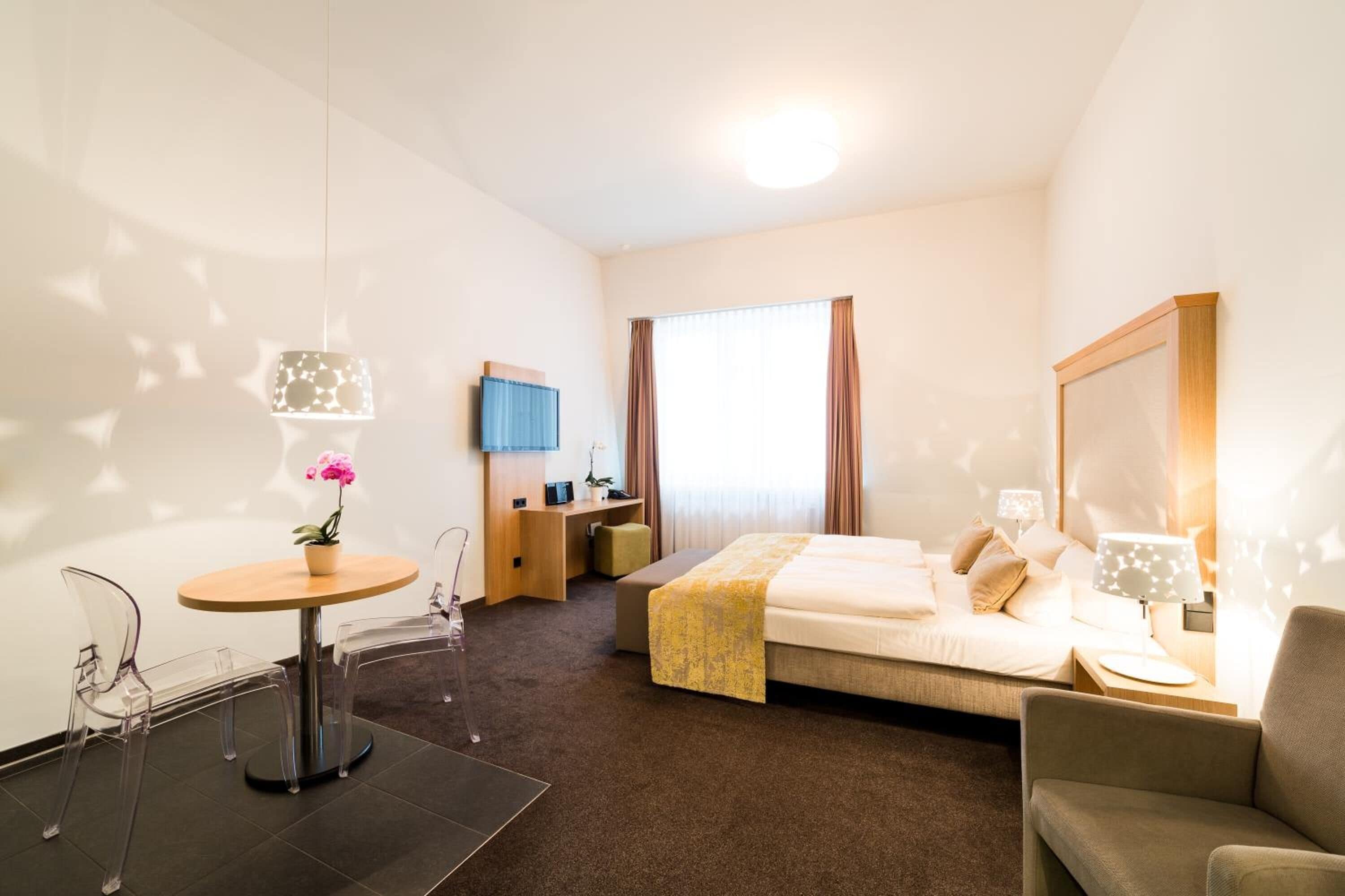 Ett hotellrum med en säng, ett skrivbord, en stol, ett litet bord och en tv.