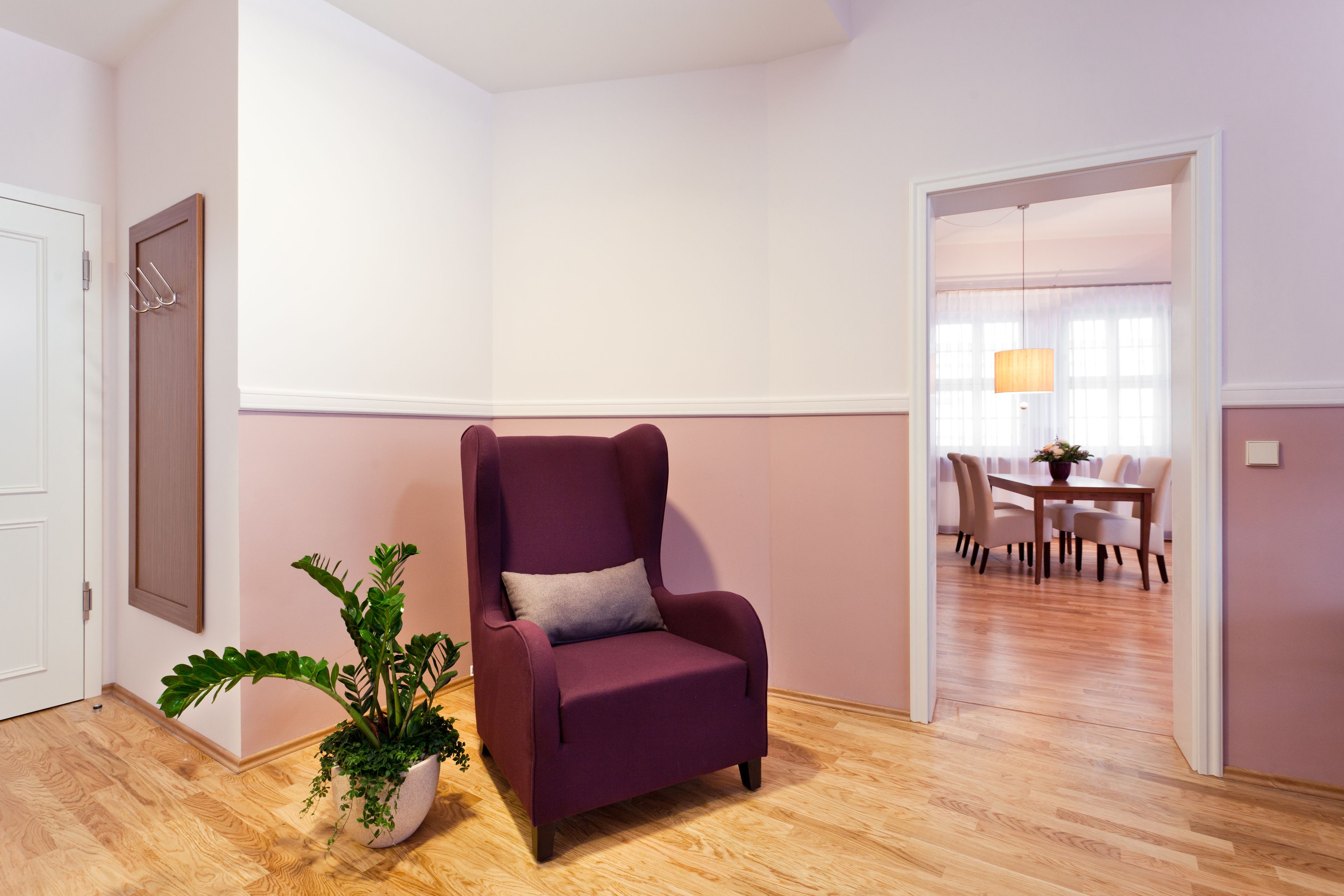 A room with a purple armchair, a potted plant, and a dining area visible through an open door.