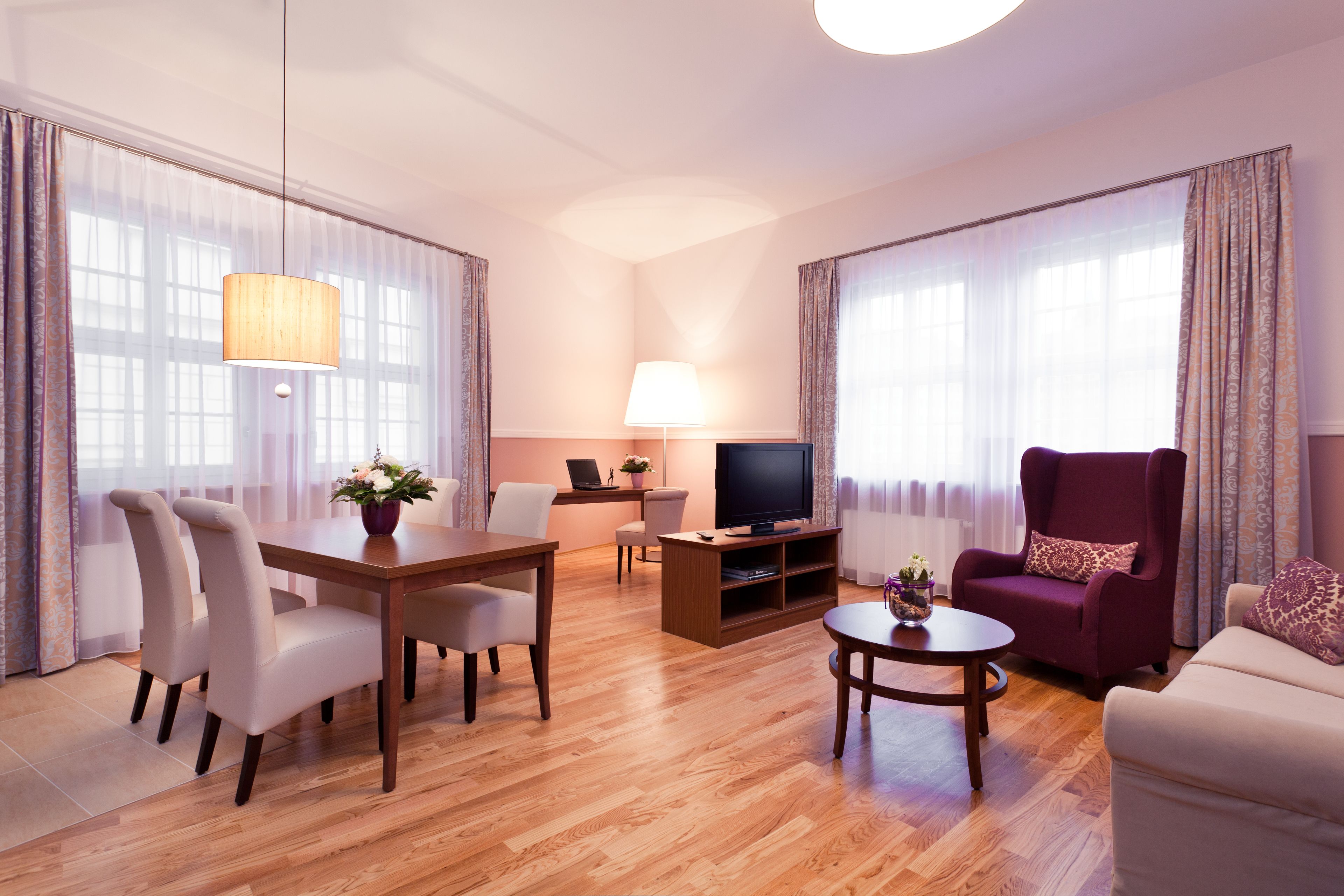 Una sala moderna con una mesa de comedor de madera, dos sillas, un sofá, un televisor y una lámpara.