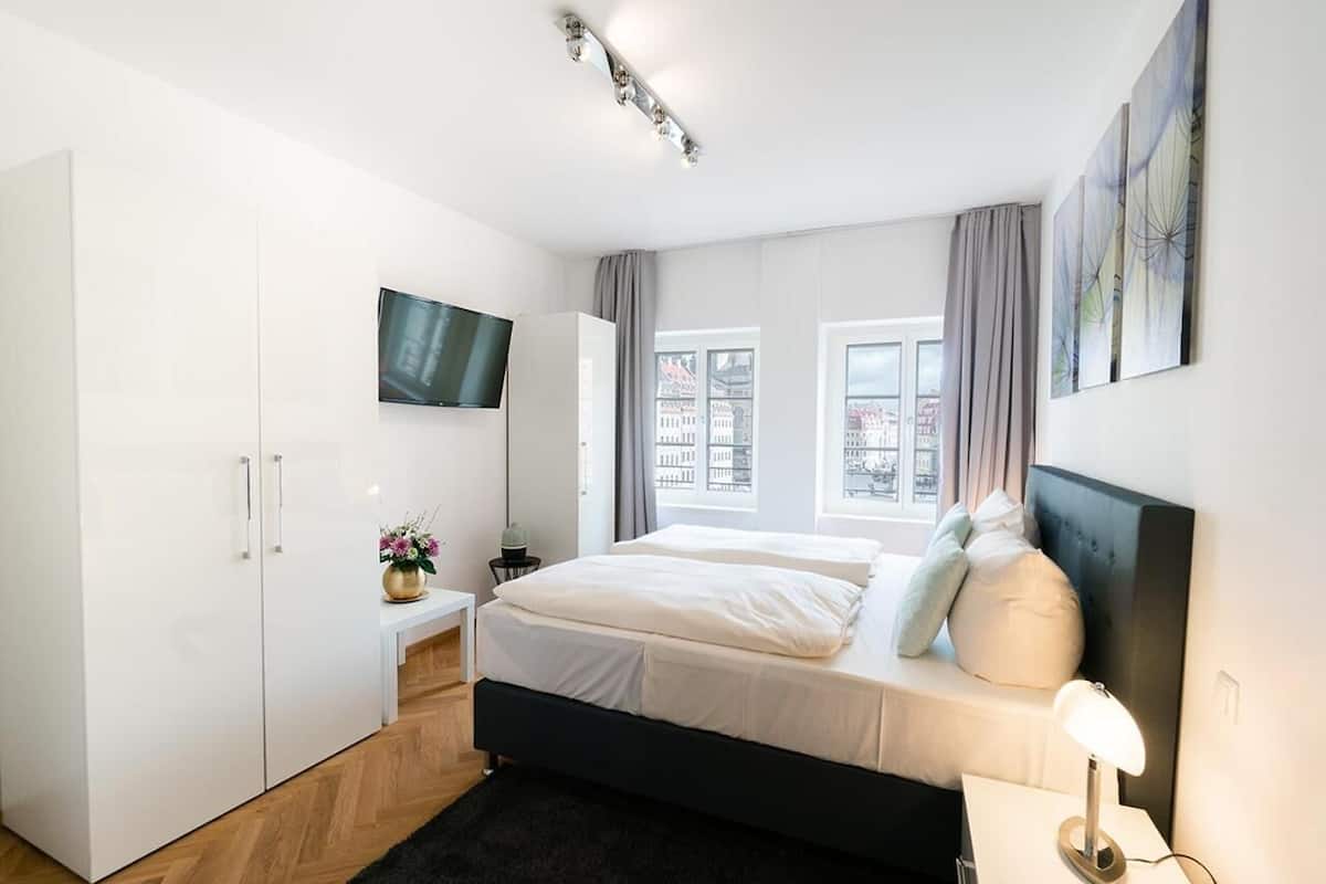 Ein modernes Schlafzimmer mit einem großen Bett, einem Kleiderschrank, einem Flachbildfernseher und einem Fenster mit Blick auf die Stadt.