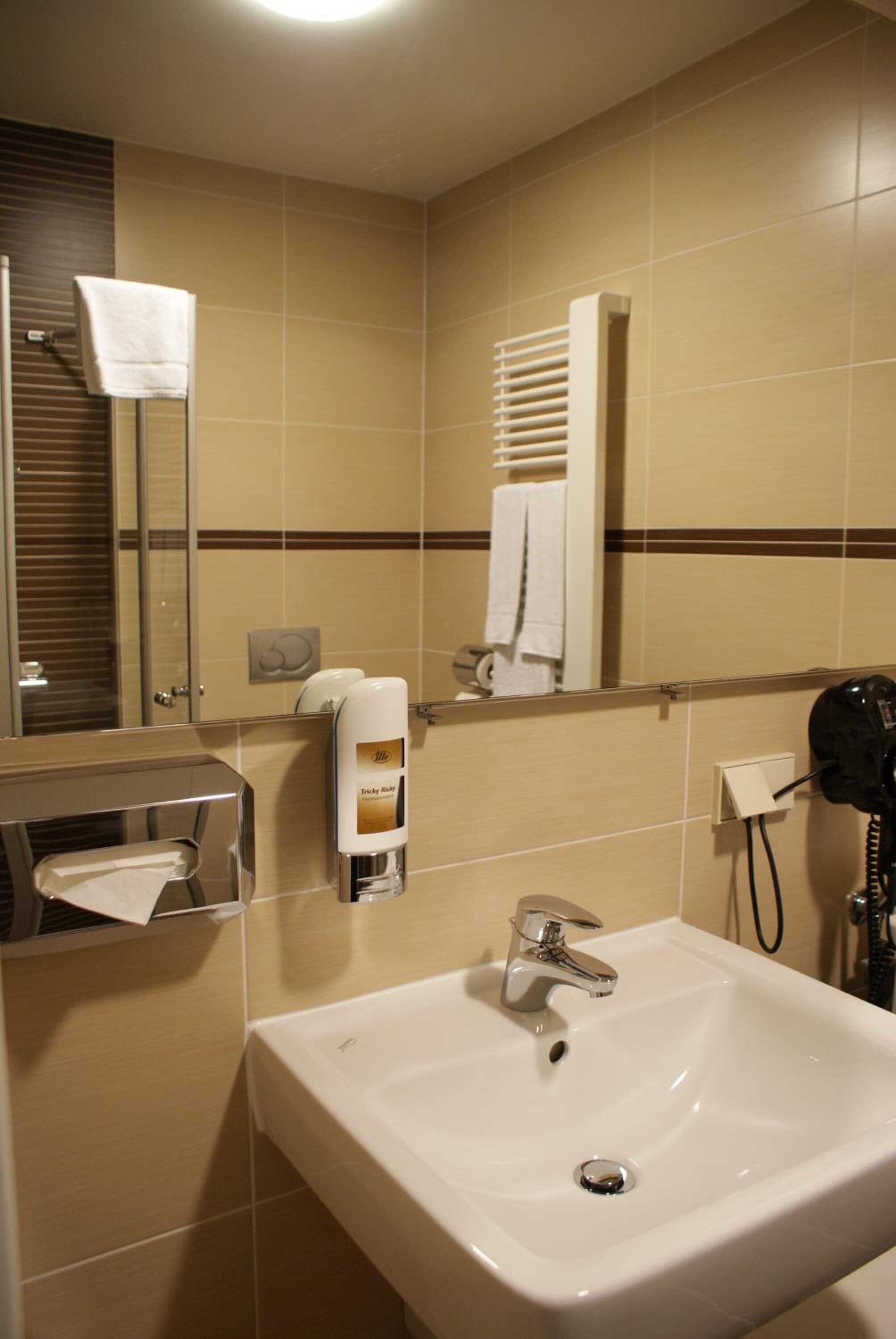 A bathroom with a sink, mirror, towel dispenser, and hairdryer.