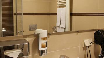 Une salle de bain équipée d’un lavabo, d’un miroir, d’un distributeur de serviettes et d’un sèche-cheveux.