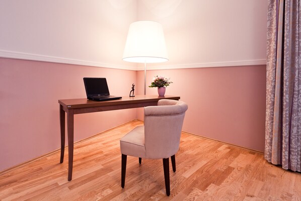 A room with a wooden desk, a laptop, a lamp, a chair, and a small plant. - Aparthotel am Schloss (Dresden)
