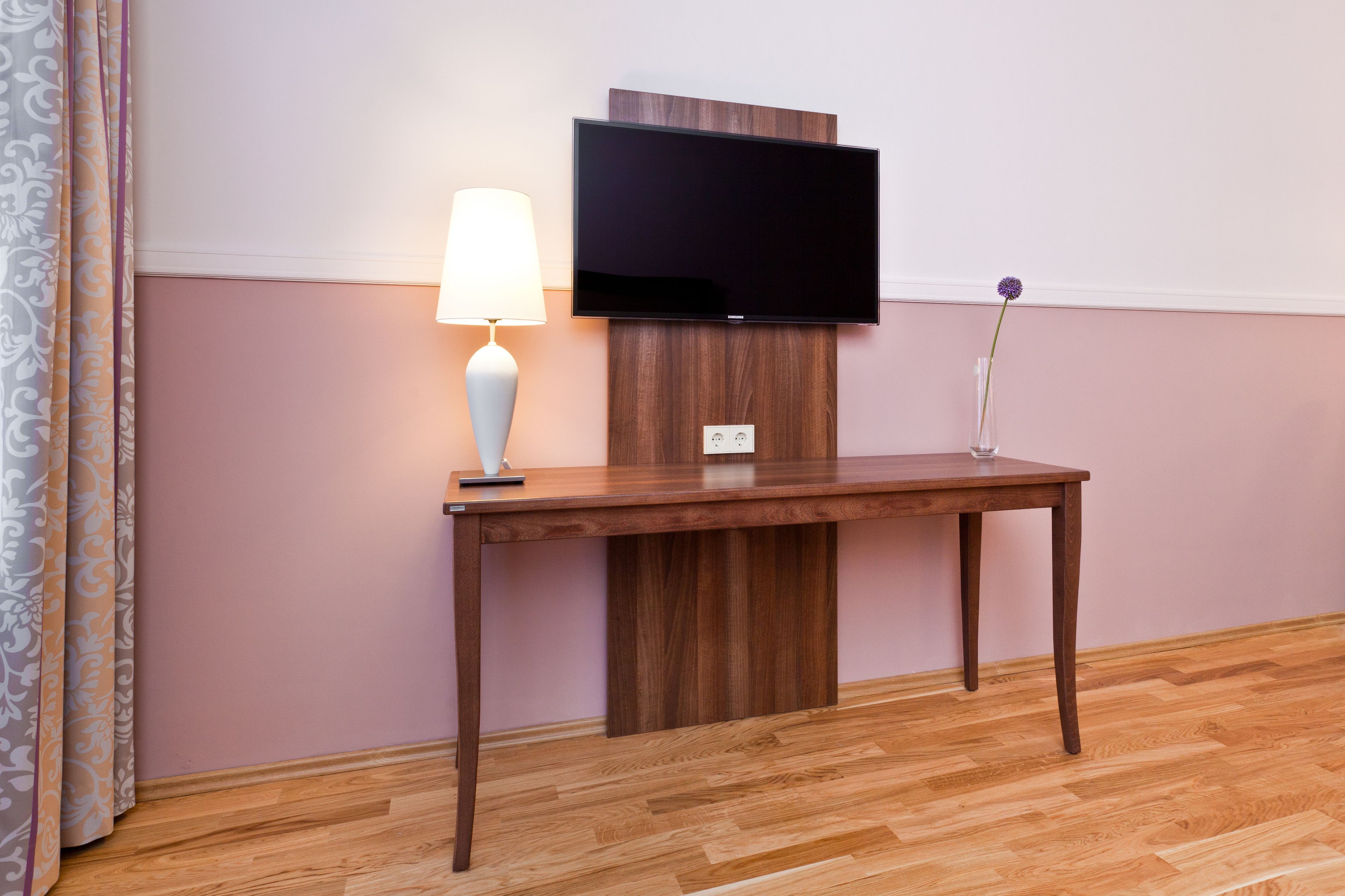 Una mesa de madera con una lámpara y un televisor de pantalla plana montado en la pared.