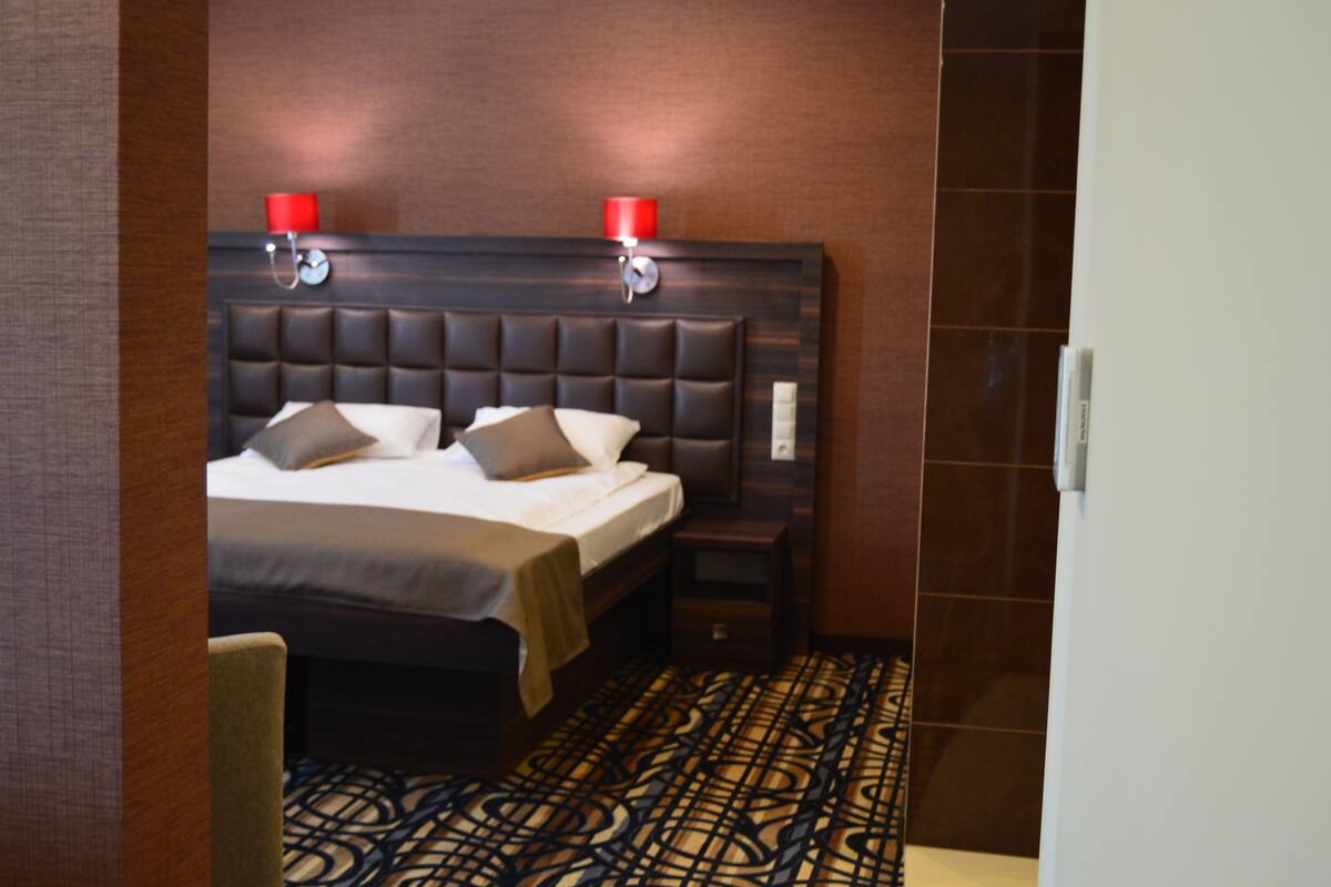 Una habitación de hotel con una cama grande, dos lámparas de noche, una mesita de noche y una alfombra estampada.