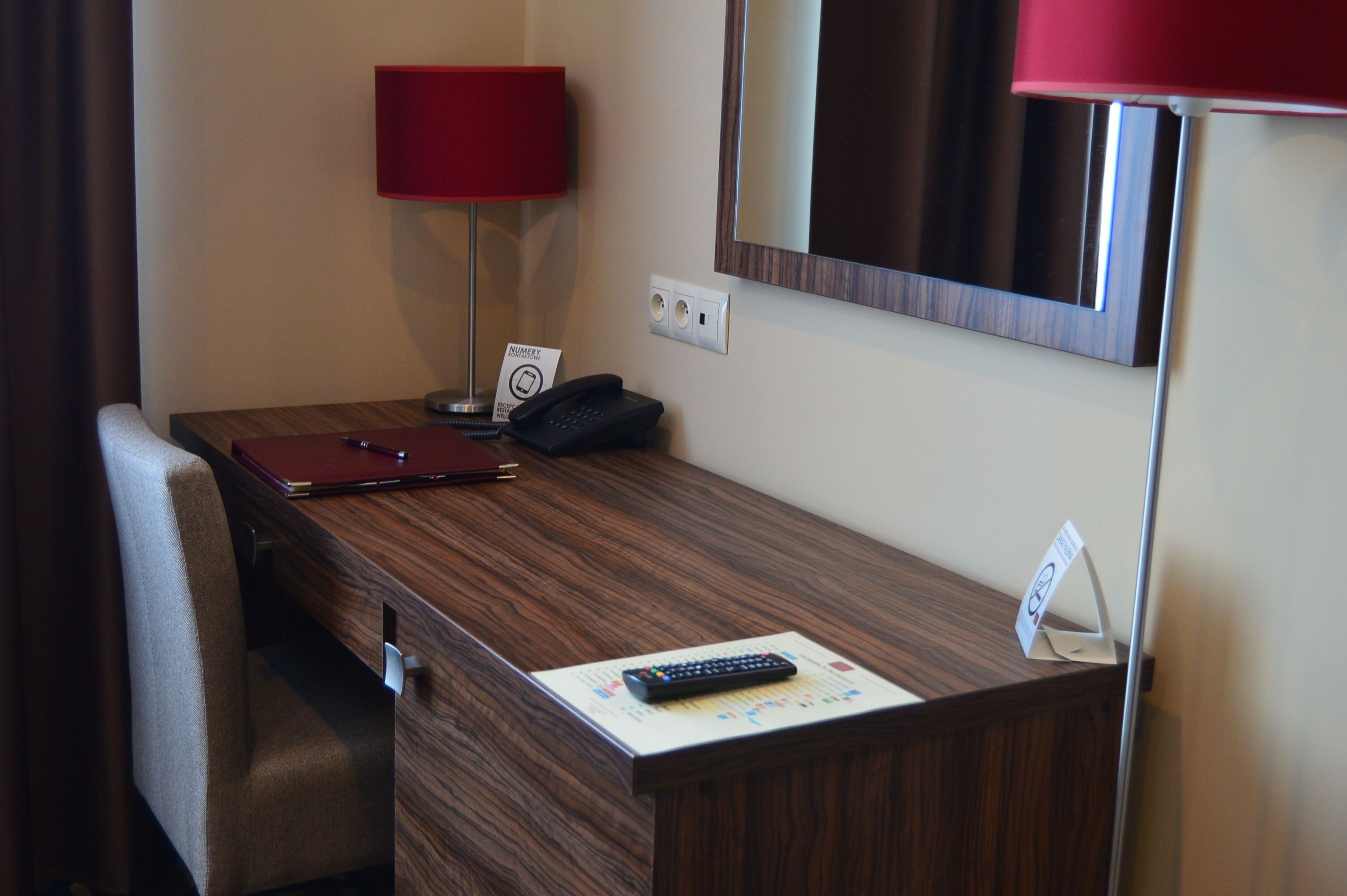 A hotel room desk with a red lamp, a telephone, a remote control, and a sign indicating a minibar.