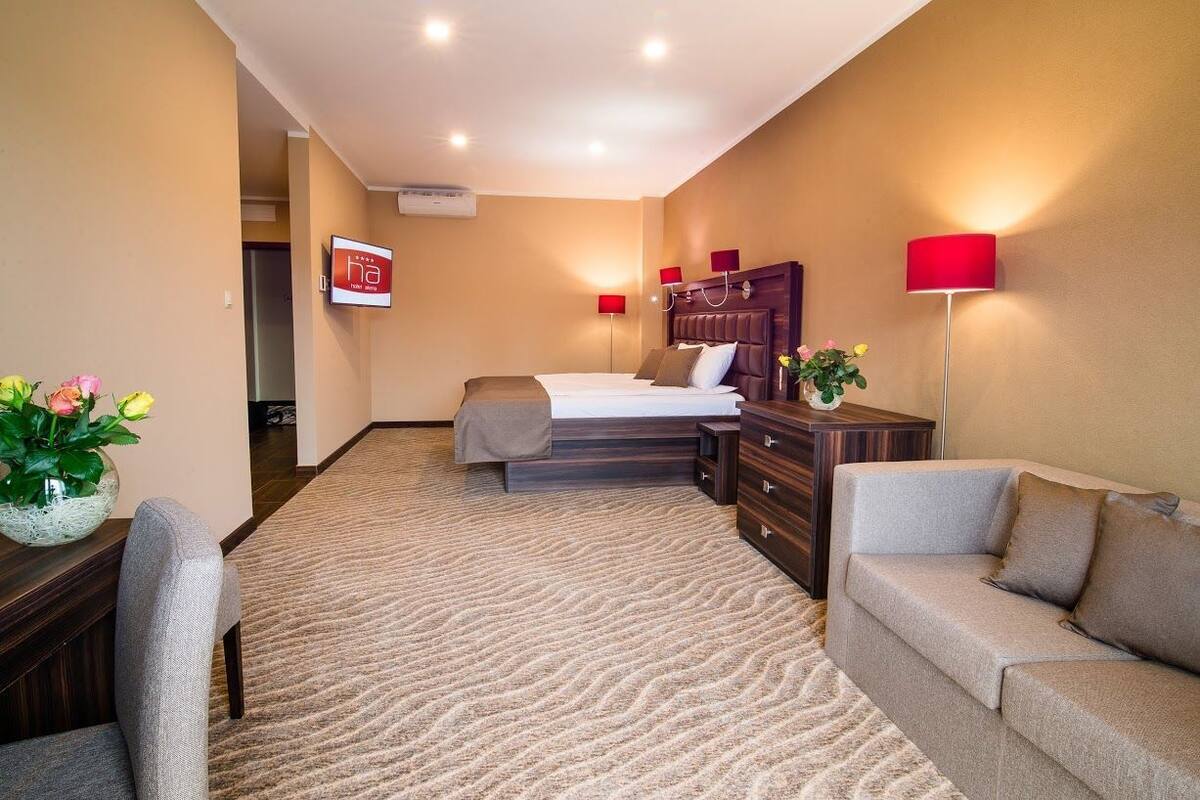 Habitación de hotel con cama, sofá, escritorio con cajones, televisor y una lámpara roja.
