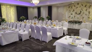 Un salón de banquetes con mesas redondas, sillas blancas y centros de mesa florales.