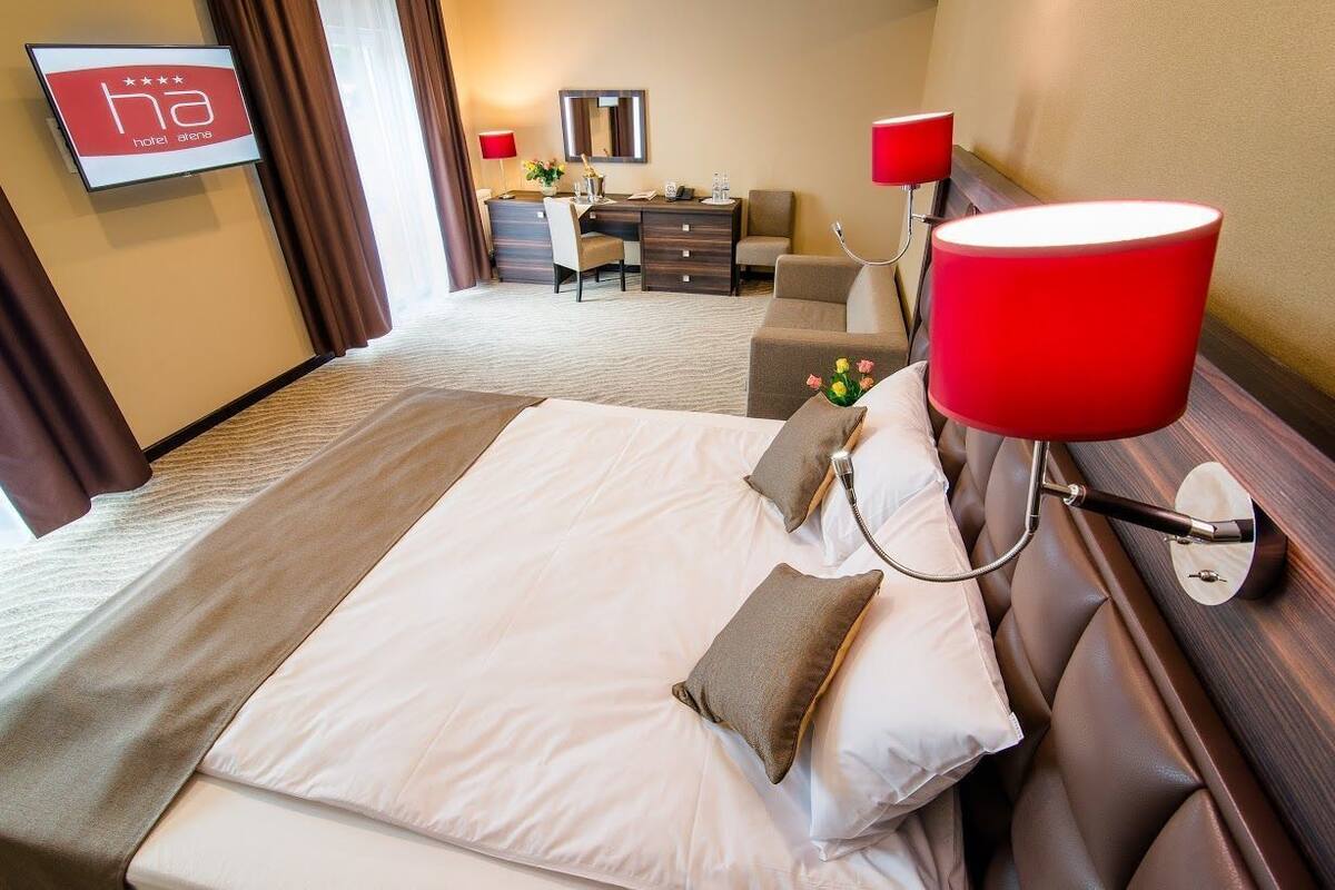 Una habitación de hotel con cama, escritorio, silla, televisor y una lámpara roja.