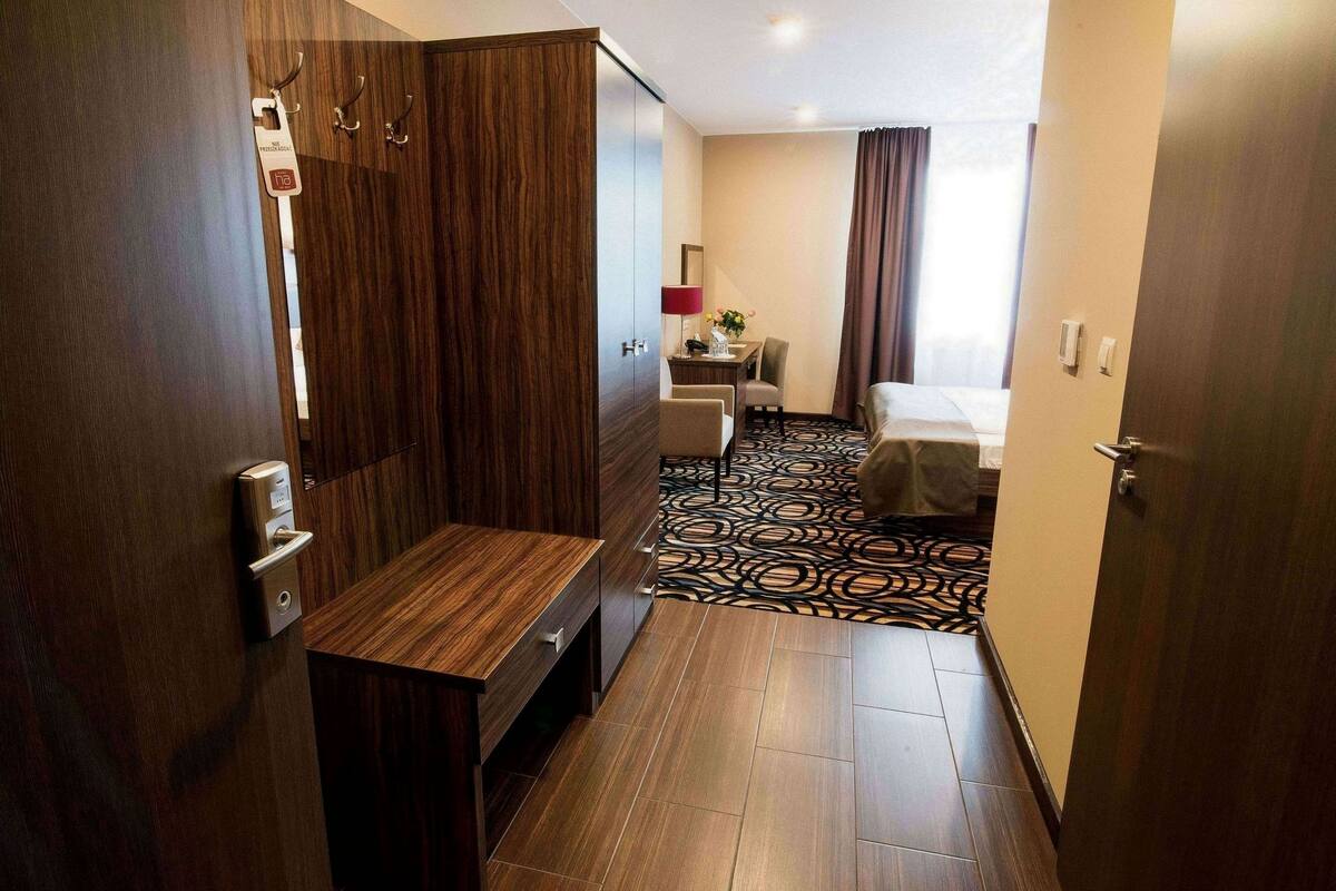 Una habitación de hotel con un armario de madera, un escritorio, una silla, una cama y una alfombra estampada.