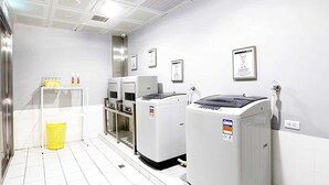 A laundry room with white tiled floors, a yellow basket, and two large white washing machines. - Royal Group Hotel Bo Ai Branch (Kaohsiung)
