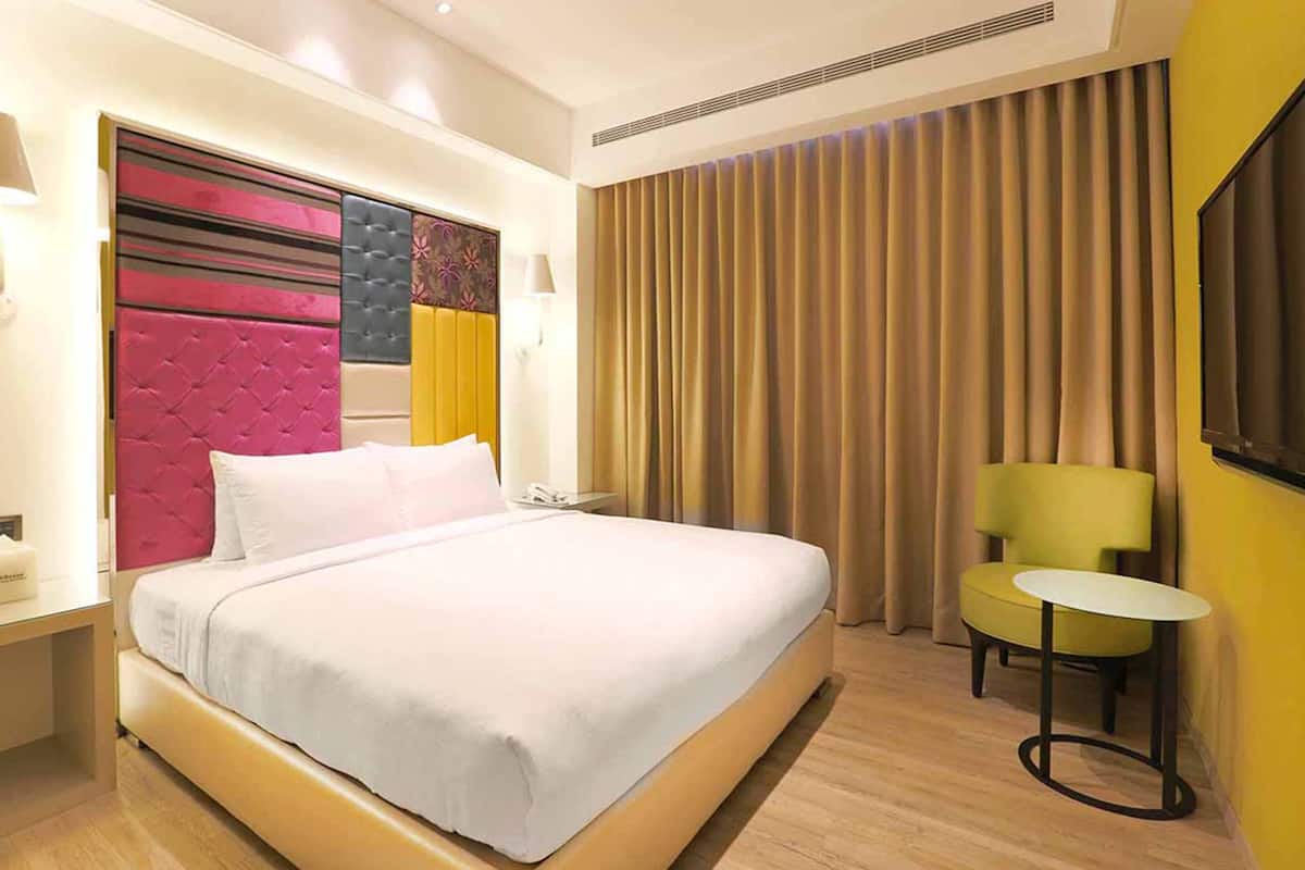 A hotel room with a large bed, a small table, a chair, and a window with curtains.