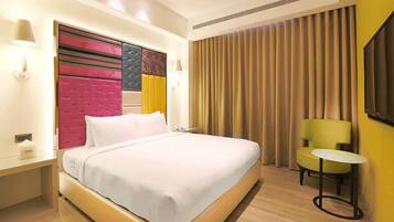 A hotel room with a large bed, a small table, a chair, and a window with curtains.