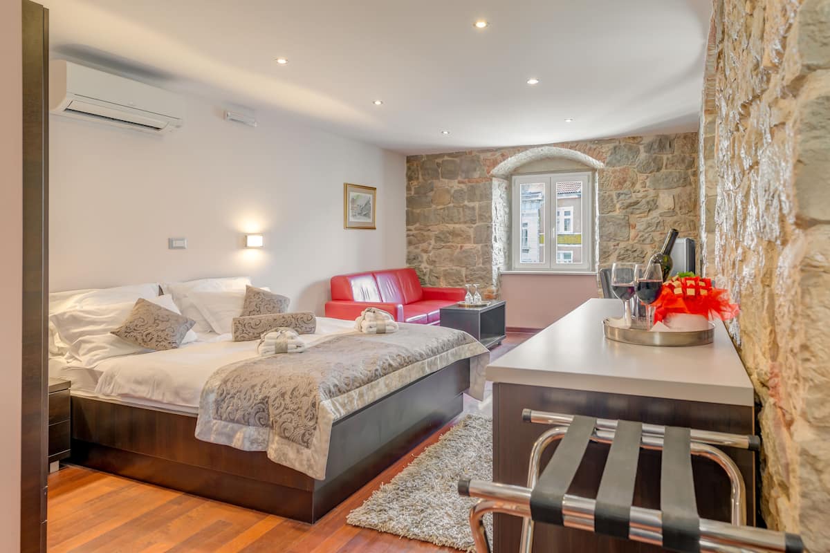 A modern bedroom with a bed, a red sofa, a desk with a chair, and a stone wall.