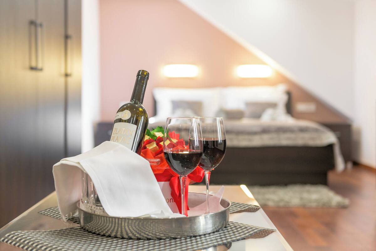 Une bouteille de vin, deux verres à vin et un cadeau emballé, le tout disposé sur un plateau dans une chambre d’hôtel.