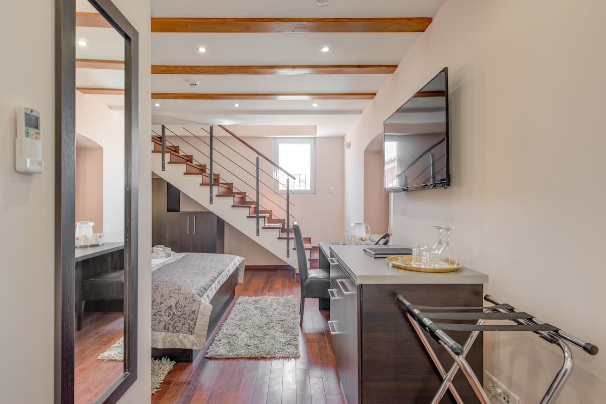 A modern bedroom with a wooden staircase, a bed, a desk, and a mirror.