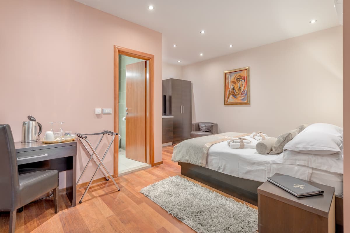 A bedroom with a bed, a desk, a chair, a radiator, and a painting on the wall.
