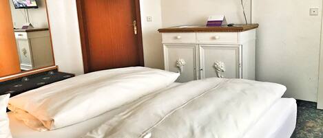 Une chambre d’hôtel avec deux lits, une porte en bois, un téléviseur fixé au mur et une commode avec un miroir.
